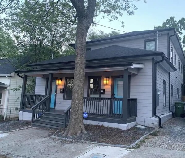 A two-story house with a porch, a tree in front, and a street view.