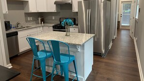 A modern kitchen with white cabinets, a stainless steel refrigerator, a granite countertop, and two blue bar stools. - Rare Find! 6 Bedroom Duplex, Close to Downtown! (Atlanta)