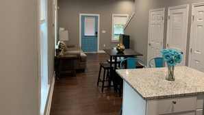 A modern kitchen with granite countertops, a dining area with a blue chair, and a living room with a sofa and lamp. - Rare Find! 6 Bedroom Duplex, Close to Downtown! (Atlanta)