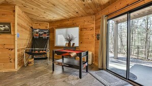 A wooden interior with a pool table, a basketball hoop, and a large sliding glass door leading to an outdoor area. - A Tucked Away Lodge | Ellijay, GA (Ellijay)