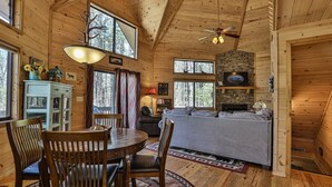 A wooden cabin interior with a dining area, sofa, fireplace, and large windows. - A Tucked Away Lodge | Ellijay, GA (Ellijay)