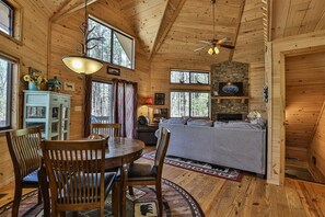 L’intérieur d’un chalet en bois comprend un coin repas, un canapé, une cheminée et de grandes fenêtres.