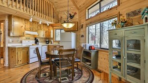A wooden cabin interior with a dining area, kitchen, and a large window. - A Tucked Away Lodge | Ellijay, GA (Ellijay)