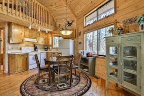 A wooden cabin interior with a dining area, kitchen, and a large window.