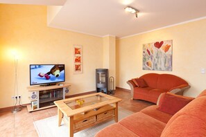 Uma sala de estar com televisão, sofá e um quadro decorativo.
