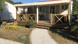A covered outdoor area with a wooden deck, a small table with chairs, and a gravel path leading to a building. - Chalet in a private park in Saint Pierre D'oléron (Saint-Pierre-d'Oléron)