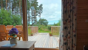 Una terraza de madera con mobiliario exterior, una planta en maceta y vistas a un paisaje boscoso.