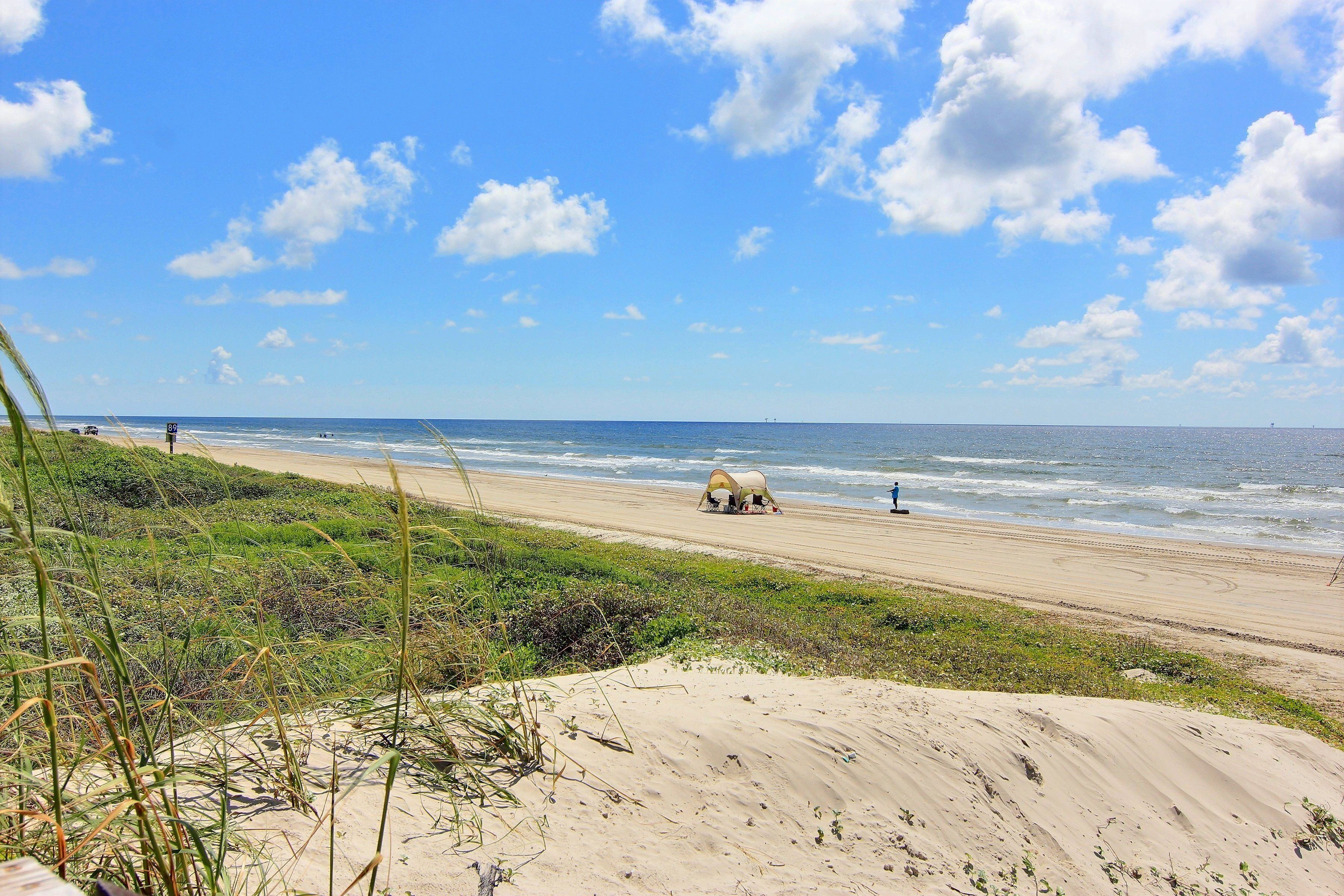 A beach with a dune, a tent, and the ocean.