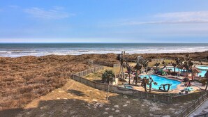 A beachside resort with a swimming pool, palm trees, and a wooden walkway leading to the beach.