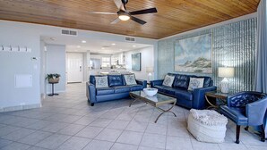 A spacious living room with a blue leather sofa set, a glass coffee table, and a decorative lamp.