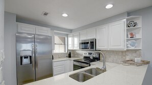 A modern kitchen with white cabinetry, stainless steel appliances, a built-in microwave, and a stainless steel sink.