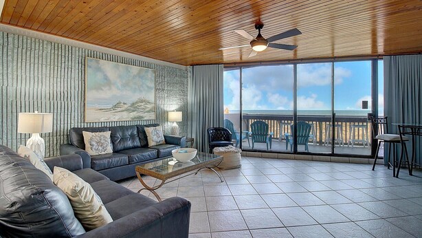 A spacious living room with a large window offering a view of the beach, a ceiling fan, and a cozy seating area with a coffee table.