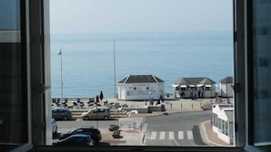A view from a window overlooking a coastal area with a road, a few cars, and a building with a white facade. - THE HORIZON (Fécamp)