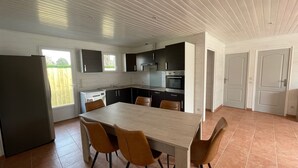 Ett modernt kök med en matplats, utrustat med ett stort bord och stolar, ett kylskåp och en diskmaskin.