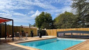 En trädgård med en pool, ett trädäck, utemöbler och ett trästaket.