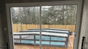 Camera da letto con un'ampia porta scorrevole in vetro che si apre su una terrazza esterna con piscina e pavimento in legno.