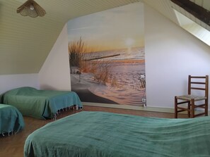 Une chambre avec deux lits, une chaise en bois et une grande fresque murale représentant une scène de plage.