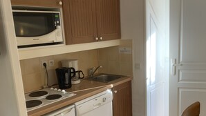 A compact kitchen with wooden cabinets, a microwave, a stove, a dishwasher, and a sink. - House in vacation village (Monflanquin)