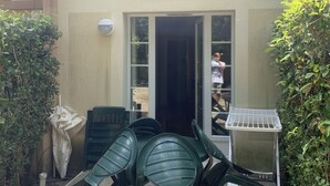 A patio area with a table and chairs, a small white table, and a potted plant. - House in vacation village (Monflanquin)