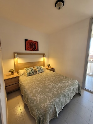 A bedroom with a bed, two bedside tables, a nightstand, a wall-mounted light fixture, a ceiling light, a window, and a door. - Luxury apartment 3 bedrooms + roof top 35 m2 Spa- jacuzzi (Empuriabrava)