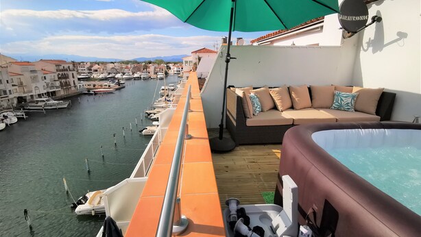 Un balcón con vista a un puerto deportivo, un sofá con cojines y un jacuzzi.
