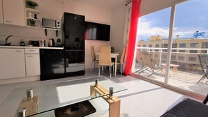 Una cocina moderna con un refrigerador negro, un microondas y una zona de comedor con una mesa y sillas de vidrio.