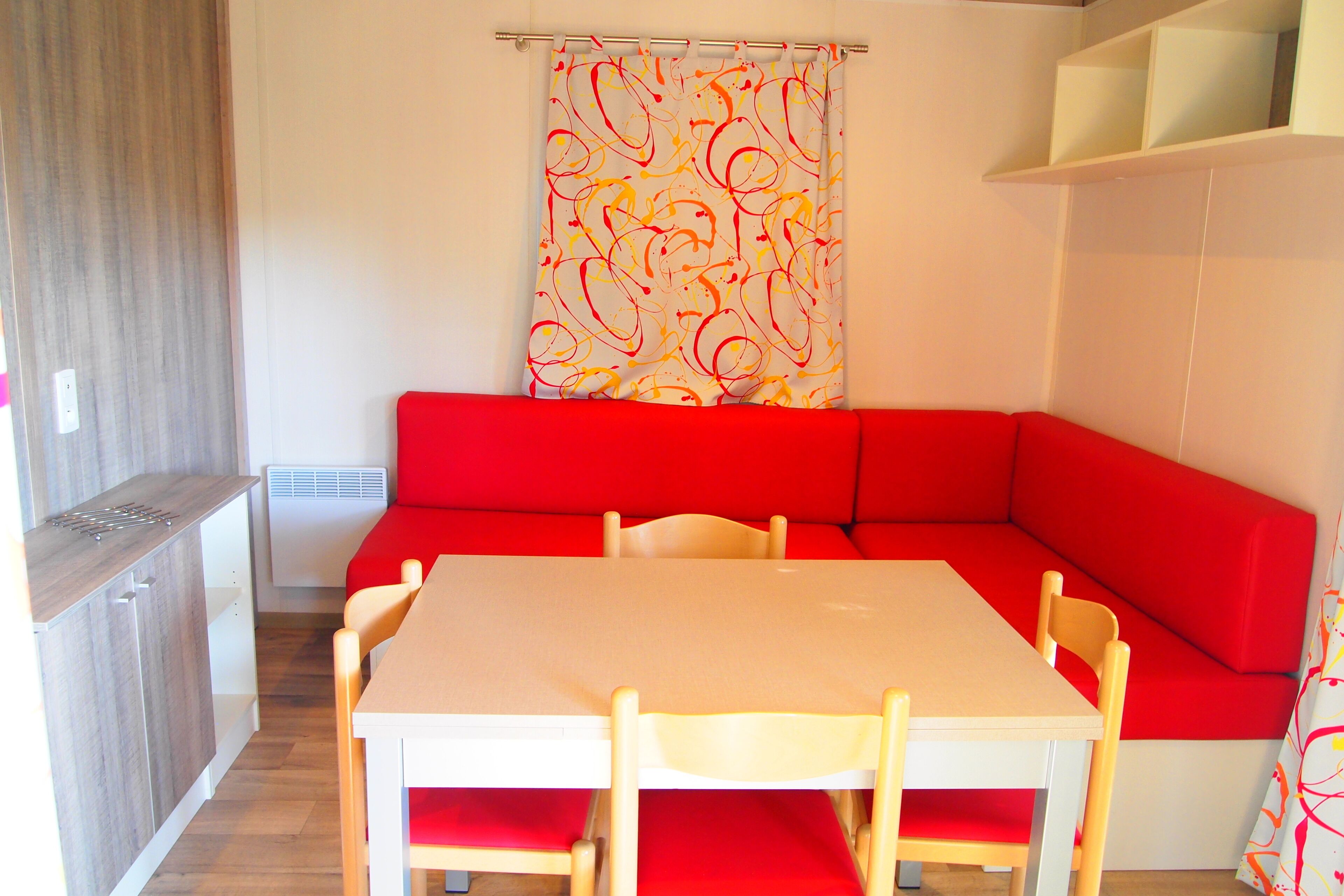 A compact living space with a red sofa, a small dining table, and a kitchenette area.