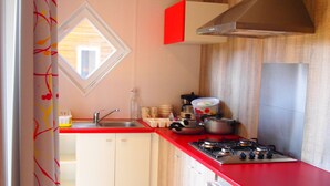 Una cocina compacta con encimera roja, armarios blancos y estufa de acero inoxidable, además de horno integrado.