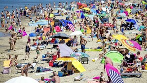 En fyldt strand med mange parasoller og mennesker.