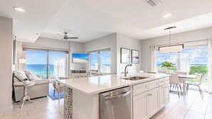 A modern kitchen with a large island, white cabinetry, and a view of the ocean. - Gulf Views ~ Lockout Unit ~ Private Foyer ~ Balcony (Miramar Beach)