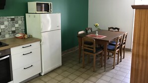 Cozinha compacta com geladeira branca, micro-ondas e mesa de jantar com cadeiras.
