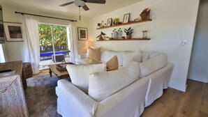 Ein Wohnzimmer mit einem weißen Sofa, einem Holztisch und Blick auf einen Pool durch eine Glastür.