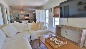 Ein Wohnzimmer mit einem weißen Ecksofa, einem Couchtisch aus Holz mit einem gewebten Korb und einem flachbildschirmfernseher an der Wand.