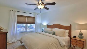Une chambre à coucher avec un lit, une table de chevet, un ventilateur de plafond et une fenêtre avec des rideaux.