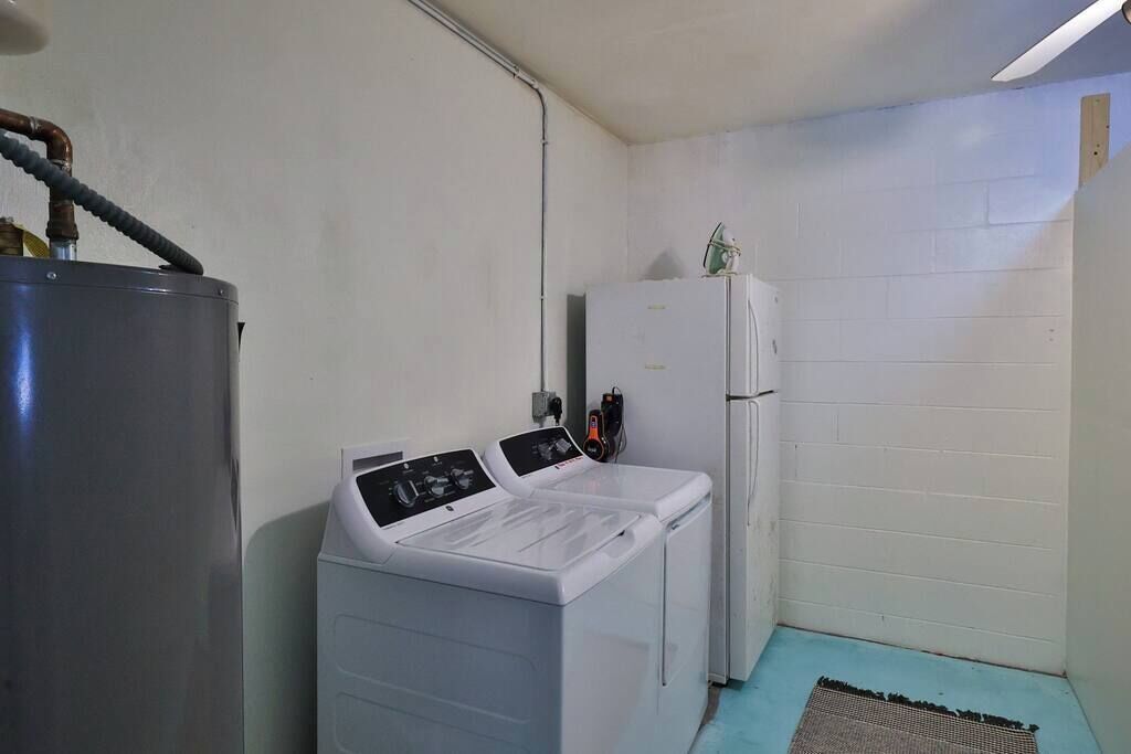 A laundry room with a large water heater, two washing machines, and a refrigerator.