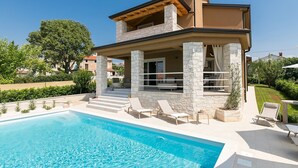 Ein modernes Haus mit zwei Etagen, einem Swimmingpool, Steinsäulen und einer Terrasse.