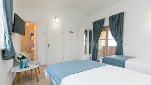 Ein Hotelzimmer mit zwei Betten, einem an der Wand befestigten Fernseher, einem kleinen Tisch mit einem Blumenstrauß und einer Tür zu einem Badezimmer.