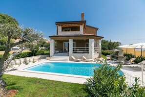 Una casa a due piani con piscina, colonne in pietra e un portico coperto.
