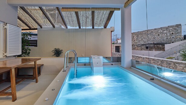 Ein Pool auf dem Dach mit einem Holztisch und Stühlen, einer Steinmauer und Blick auf die Stadt.