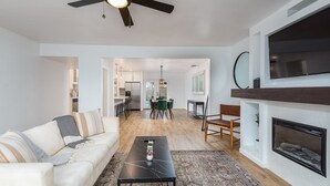 Un salon moderne avec un canapé, une table basse et une cheminée. On aperçoit à l’arrière-plan un coin repas avec une table et des chaises.