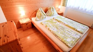 A wooden-paneled bedroom with a bed, two nightstands, a wooden dresser, and a window with curtains. - Ferienwohnung 50 m² (Kötschach-Mauthen)