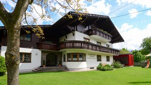 A traditional chalet-style building with a sloped roof, wooden balconies, and a well-maintained lawn. - Ferienwohnung 50 m² (Kötschach-Mauthen)