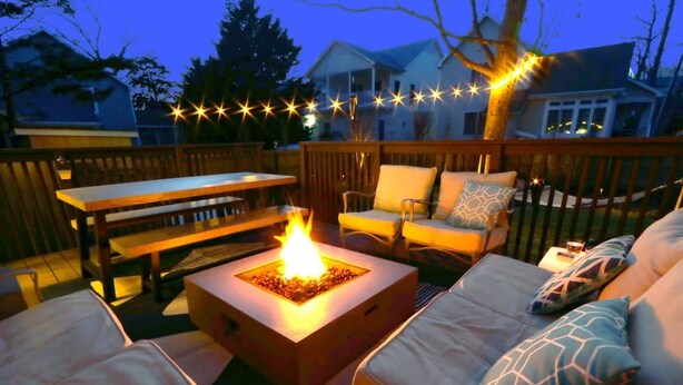 Une terrasse extérieure dotée d’un foyer, de sièges et de guirlandes lumineuses.