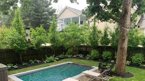 Une piscine rectangulaire, bordée d’une terrasse carrelée, entourée d’une pelouse verdoyante et d’arbres.