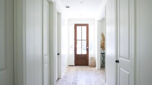 Un corridoio con porte bianche, una porta in legno in fondo e un pavimento chiaro.