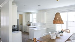 Una cucina moderna con mobili bianchi, un'isola centrale e un'area pranzo con sedie in vimini.