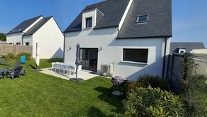 Une maison moderne à deux étages, dotée d’une pelouse bien entretenue, d’un espace extérieur aménagé pour se détendre et d’un patio couvert.