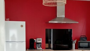Une cuisine moderne avec un mur rouge, des armoires blanches, une table à manger en bois et des chaises noires.