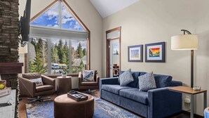 Un salon moderne avec une grande fenêtre, un canapé bleu, un fauteuil en cuir marron et une table basse.