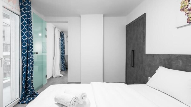 Moderni hotellihuone, jossa on suuri sänky, vaatekaappi ja lasiovi, joka johtaa parvekkeelle.